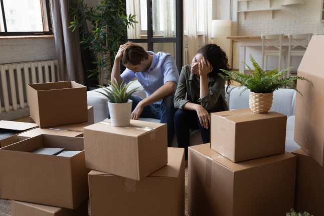 Unhappy frustrated couple sitting on couch with cardboard boxes, eviction