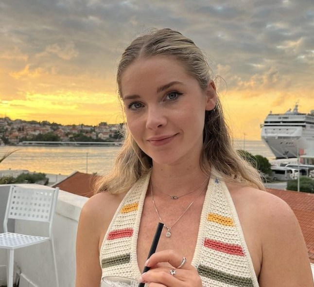 Woman with cocktail sitting on terrace bar with sunset behind her